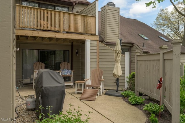 back of property with a balcony, a chimney, a patio area, and roof with shingles