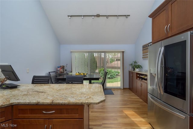 kitchen with stainless steel fridge, rail lighting, light wood finished floors, brown cabinetry, and light stone countertops