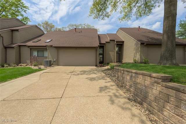 mid-century inspired home featuring concrete driveway, a garage, a front lawn, central air condition unit, and roof with shingles