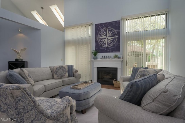 living area with high vaulted ceiling, a glass covered fireplace, and a skylight