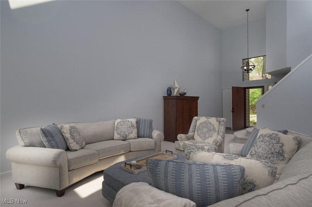 carpeted living area featuring high vaulted ceiling and a chandelier
