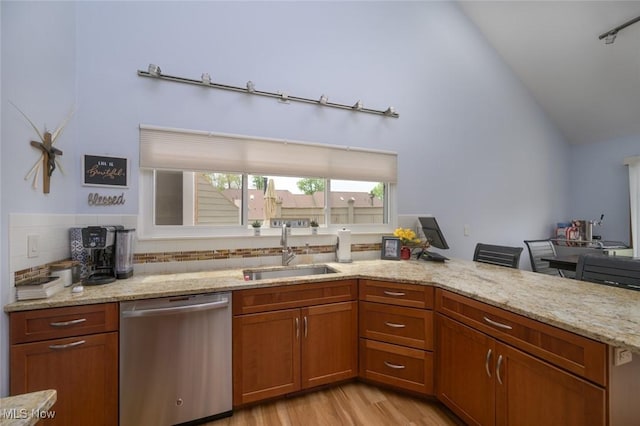kitchen with dishwasher, a sink, light stone counters, light wood-type flooring, and decorative backsplash
