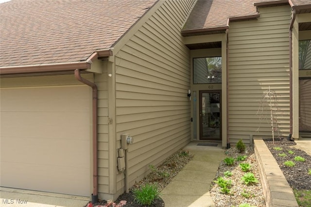 doorway to property featuring a shingled roof and an attached garage