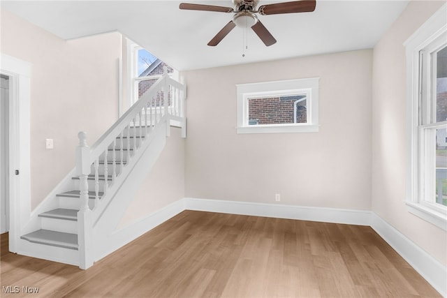 staircase featuring wood finished floors, plenty of natural light, a ceiling fan, and baseboards