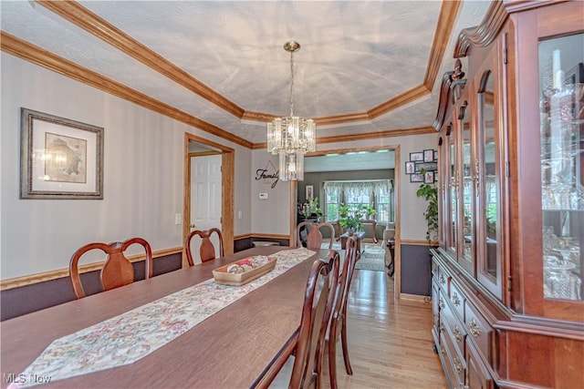 dining room featuring a chandelier, a raised ceiling, light wood-style floors, baseboards, and crown molding