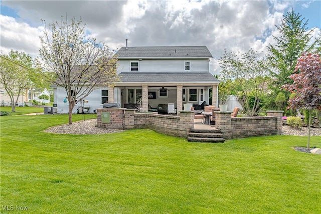 rear view of property with a lawn, ceiling fan, an outdoor living space, a patio area, and exterior kitchen