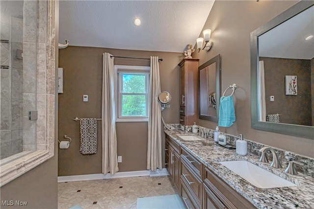 bathroom with a tile shower, double vanity, baseboards, a textured ceiling, and tile patterned flooring