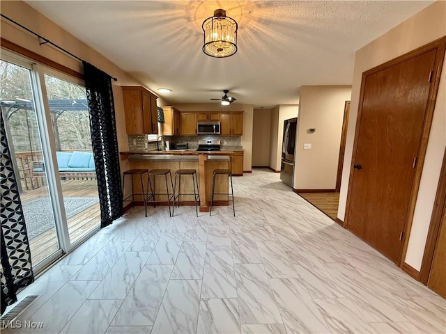36 Choctaw Trl, Malvern, OH 44644 - kitchen featuring appliances with stainless steel finishes, light marble finish floors, brown cabinetry, a peninsula, and decorative backsplash