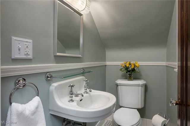 half bath with toilet, a sink, and vaulted ceiling
