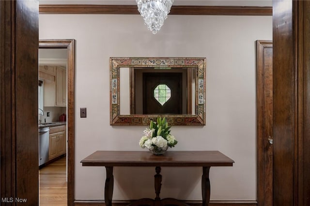 corridor featuring crown molding, a sink, a chandelier, and light wood finished floors