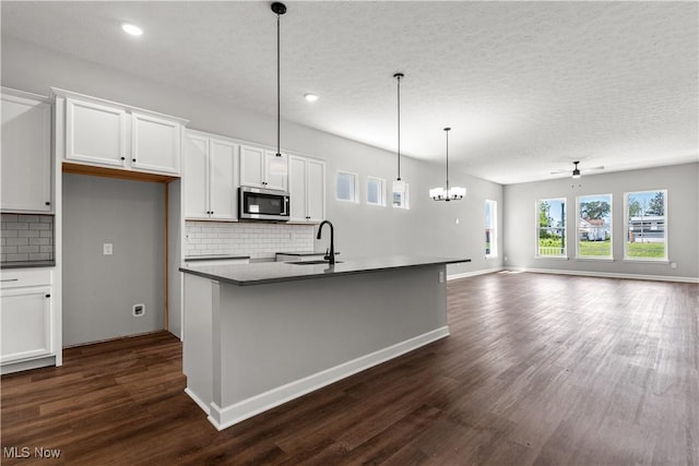 374 Bascule Dr, Lorain, OH 44052 - kitchen featuring stainless steel microwave, tasteful backsplash, dark wood finished floors, white cabinets, and a center island with sink
