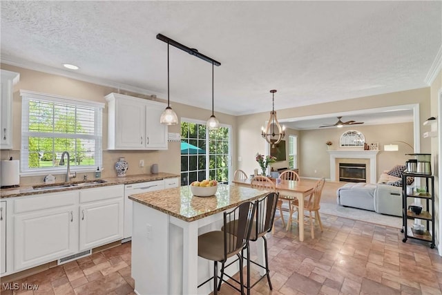 kitchen with light stone finish floors, ceiling fan, a sink, dishwasher, and a glass covered fireplace