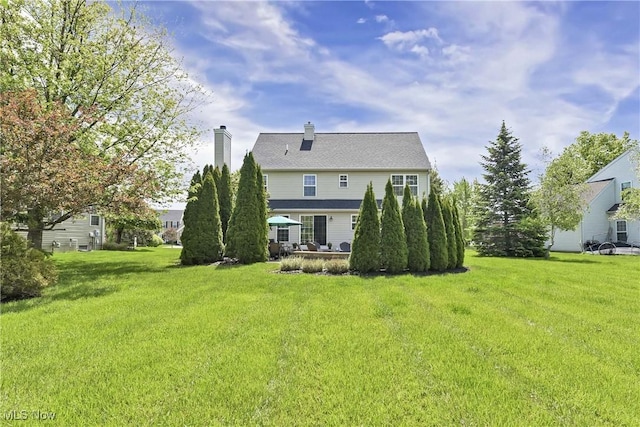 rear view of house featuring a chimney and a lawn