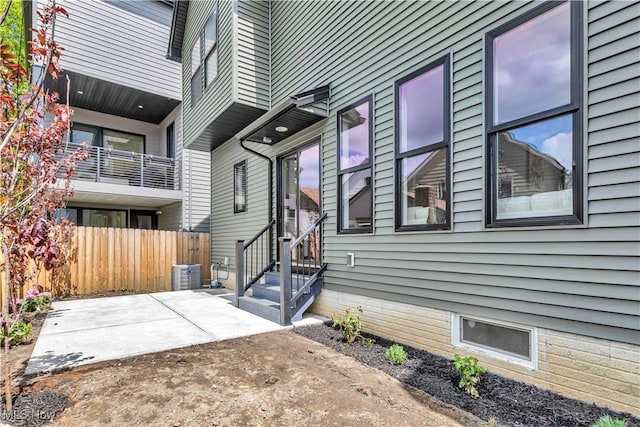 view of property exterior with fence, entry steps, central AC, and a patio area