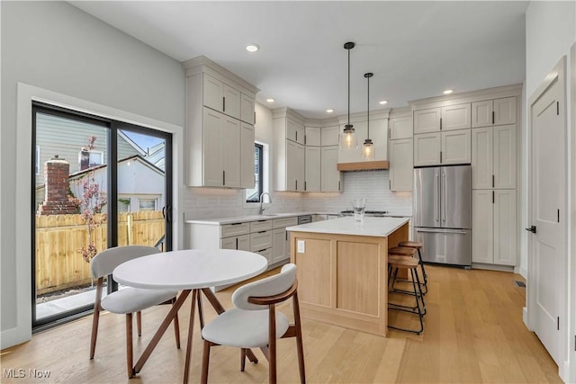 kitchen with high end refrigerator, light countertops, backsplash, a kitchen island, and light wood-style floors