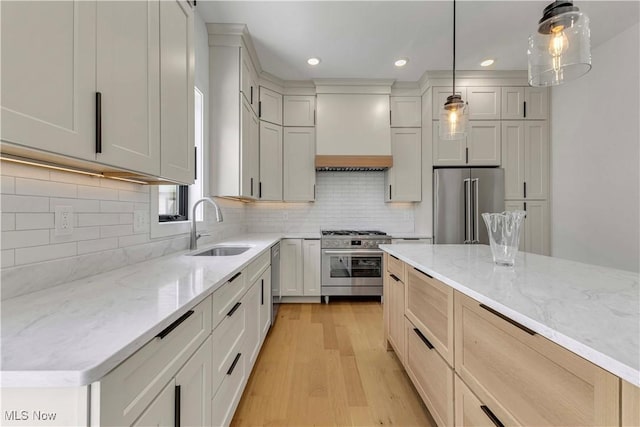 kitchen with stainless steel appliances, a sink, light wood-style floors, light stone counters, and recessed lighting