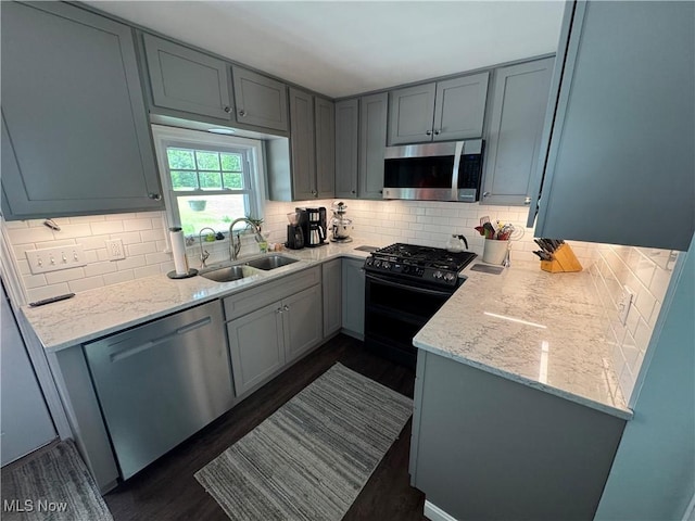 kitchen featuring appliances with stainless steel finishes, a sink, tasteful backsplash, and dark wood-style floors