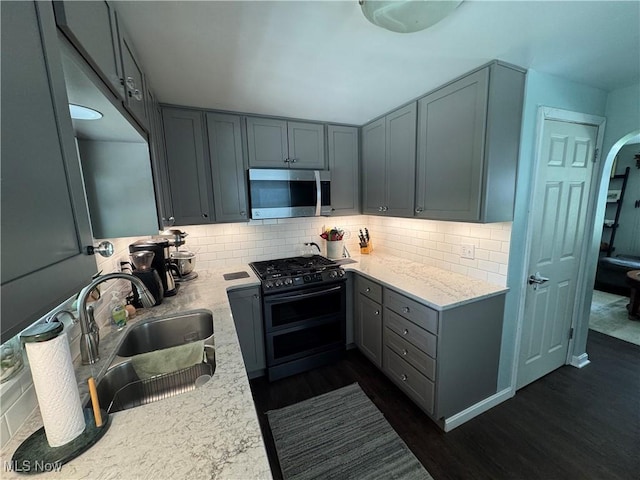 kitchen with stainless steel microwave, range with two ovens, gray cabinets, dark wood-style floors, and tasteful backsplash