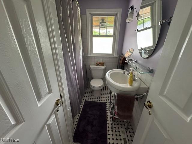 bathroom featuring a sink, tile patterned floors, toilet, a shower with curtain, and tile walls