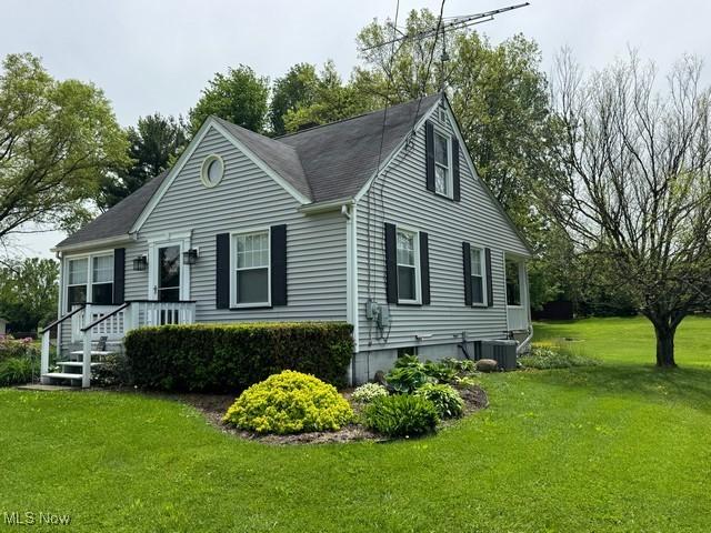 view of front of home with a front yard, central air condition unit, and a shingled roof