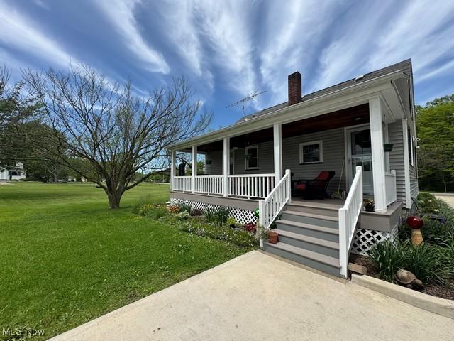 view of front of house featuring a chimney, covered porch, and a front lawn