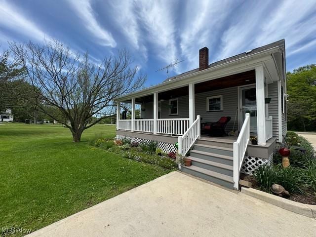 view of front of property with a chimney, covered porch, and a front yard