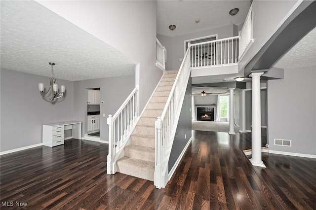 4474 Litchfield Dr, Copley, OH 44321 - stairway with wood finished floors, ornate columns, a textured ceiling, baseboards, and a warm lit fireplace
