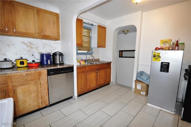 kitchen with appliances with stainless steel finishes, arched walkways, a sink, and decorative backsplash