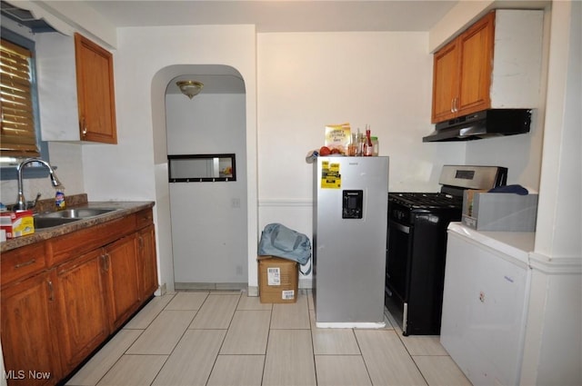 kitchen with under cabinet range hood, a sink, appliances with stainless steel finishes, brown cabinets, and arched walkways