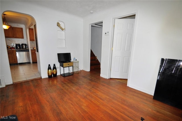 unfurnished living room featuring wood finished floors, arched walkways, baseboards, and stairs