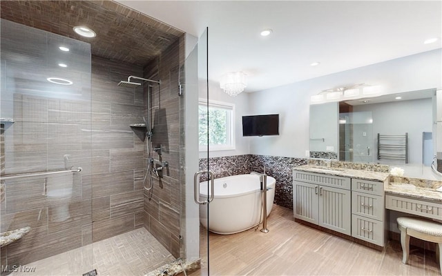 full bath with a shower stall, a freestanding bath, vanity, a towel warming rack, and recessed lighting
