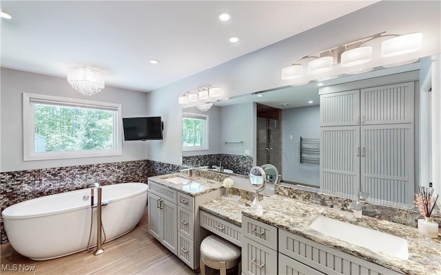 bathroom with a freestanding bath, two vanities, a shower stall, tile walls, and recessed lighting