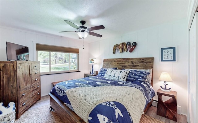 bedroom with wood finished floors, a decorative wall, and ceiling fan