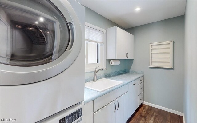 washroom featuring cabinet space, dark wood finished floors, stacked washing machine and dryer, baseboards, and recessed lighting