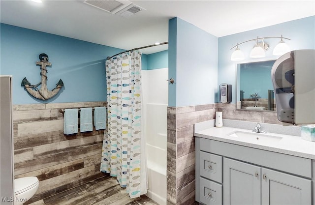 bathroom featuring tile walls, a shower with curtain, a wainscoted wall, toilet, and vanity