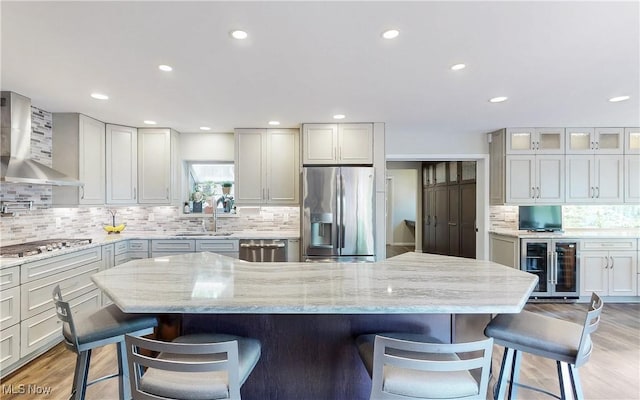 kitchen with stainless steel appliances, wall chimney exhaust hood, wine cooler, a kitchen bar, and backsplash