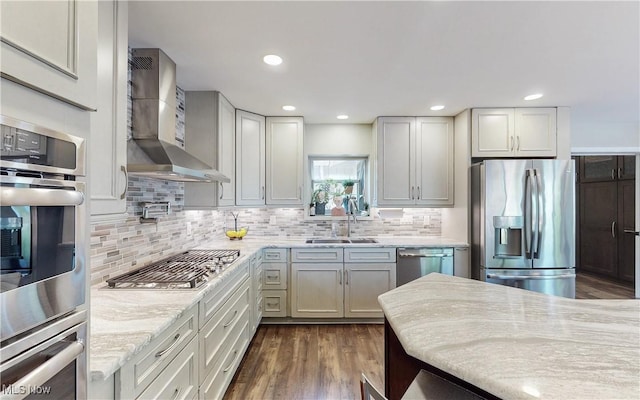 kitchen with stainless steel appliances, wall chimney range hood, a sink, decorative backsplash, and dark wood-style flooring