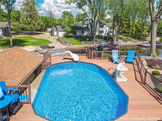 swimming pool with a water slide, a deck, and view of scattered trees