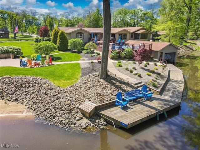 rear view of property with a lawn, a garage, an outdoor fire pit, a deck with water view, and an outbuilding