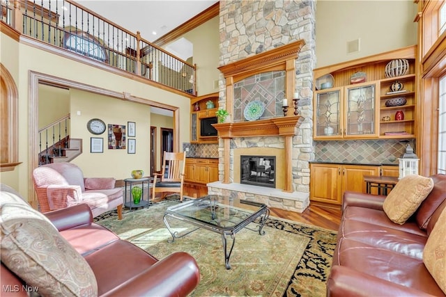 living area featuring a towering ceiling, stairway, a stone fireplace, and wood finished floors