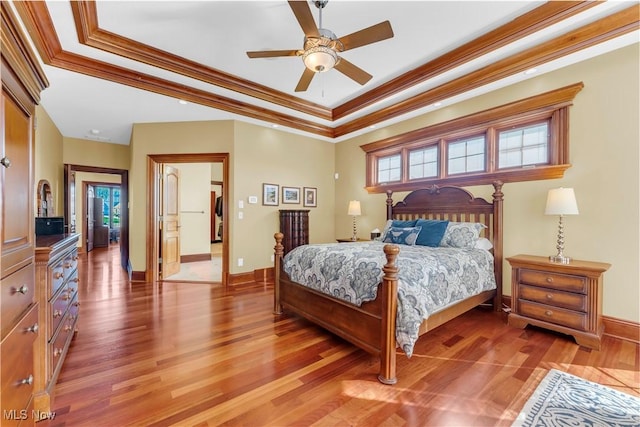 bedroom with light wood-type flooring, crown molding, a tray ceiling, baseboards, and a ceiling fan