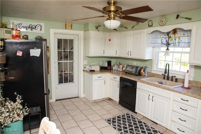 kitchen featuring freestanding refrigerator, black dishwasher, a sink, light tile patterned floors, and white cabinets
