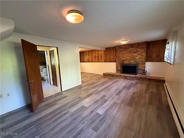 6855 Painesville Ravenna Rd, Concord, OH 44077 - unfurnished living room featuring baseboard heating, wood finished floors, a brick fireplace, and baseboards