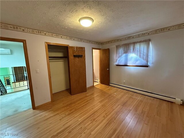 6855 Painesville Ravenna Rd, Concord, OH 44077 - unfurnished bedroom featuring a textured ceiling, baseboard heating, a closet, light wood finished floors, and a wall unit AC