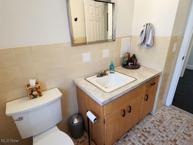 bathroom with tile walls, toilet, wainscoting, vanity, and tile patterned floors