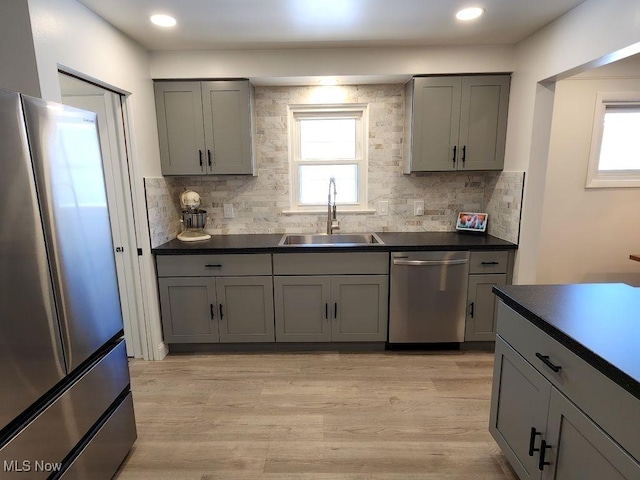 kitchen with stainless steel appliances, a sink, gray cabinetry, dark countertops, and tasteful backsplash