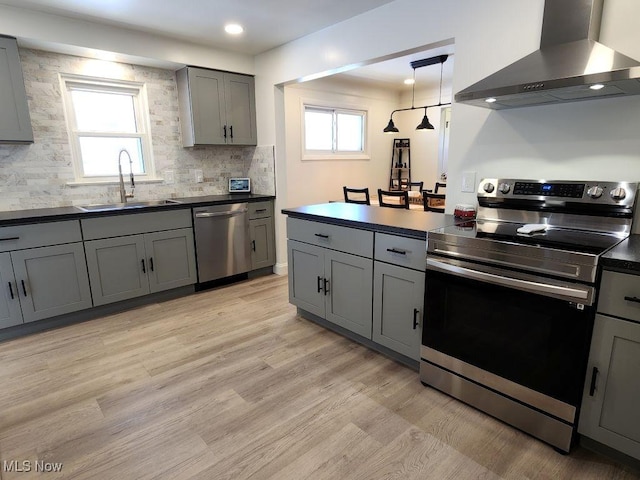 kitchen featuring stainless steel appliances, wall chimney range hood, a sink, gray cabinets, and dark countertops