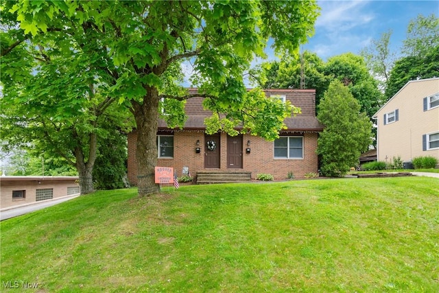 view of front of home with a front lawn, brick siding, and roof with shingles