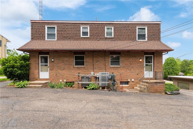 view of front of house featuring mansard roof, a shingled roof, and brick siding
