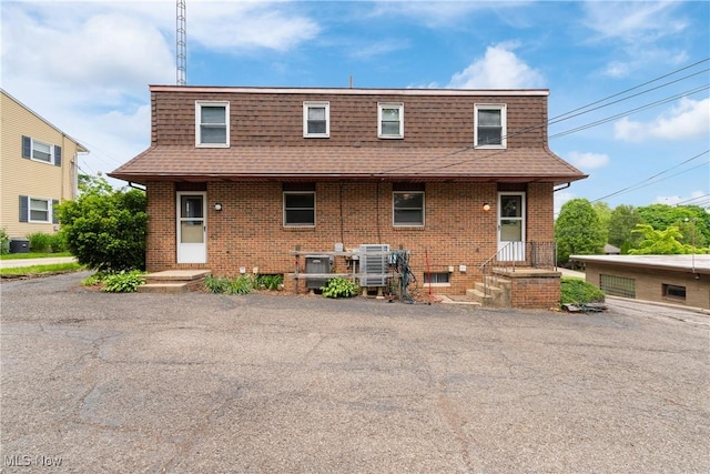view of front of property featuring mansard roof, a shingled roof, brick siding, and central AC